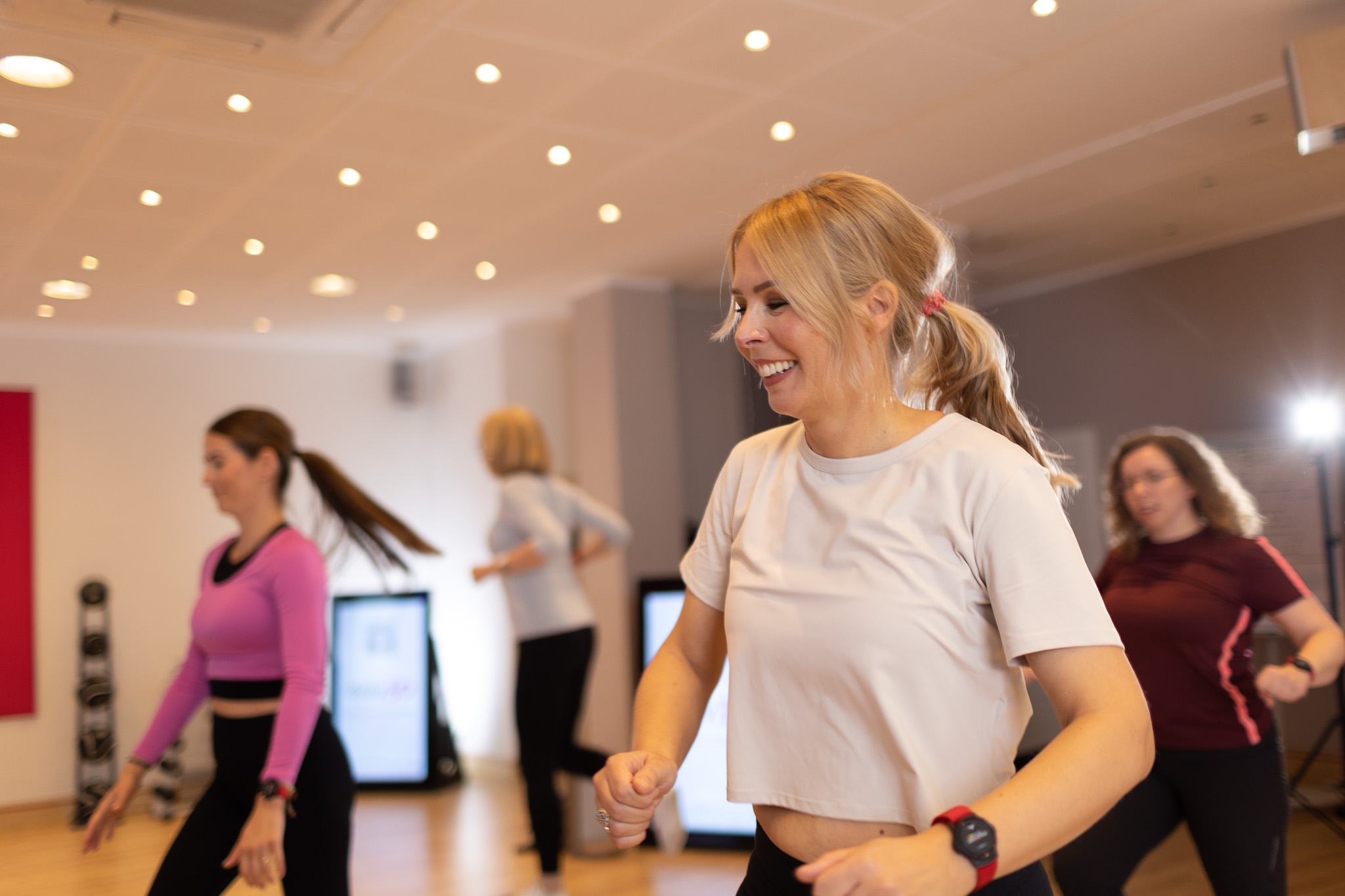 Eine junge Frau trainiert mit vielen anderen Frauen in der Gruppe. Das Workout ist körperlich fordernd, macht aber extrem viel Spaß